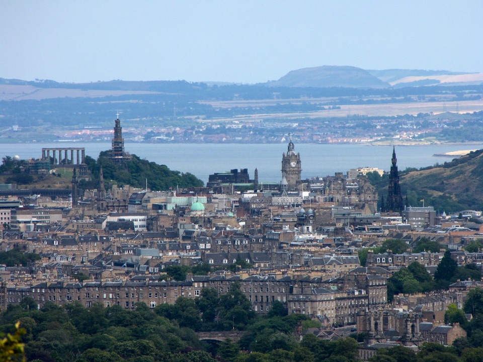 The roofs of Edinburgh seen from a hill above the city with the Firth of Forth behind
