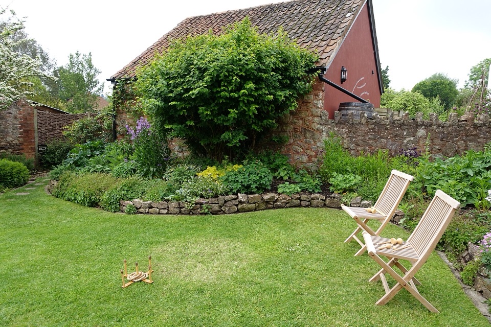 A walled back garden with a lawn, two chairs and a brick house behind