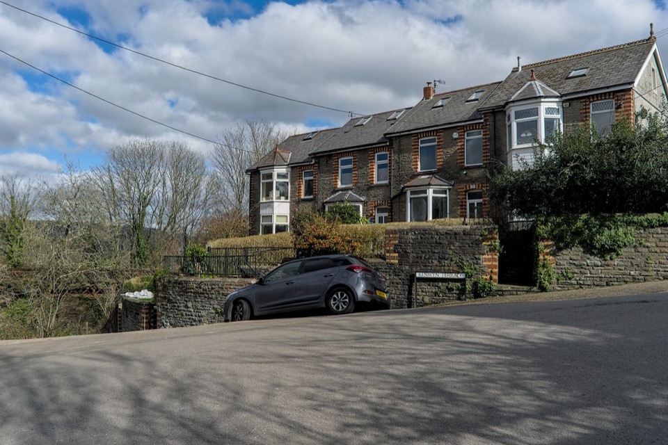 A stone terrace of houses standing above a road on a hillside in south Wales